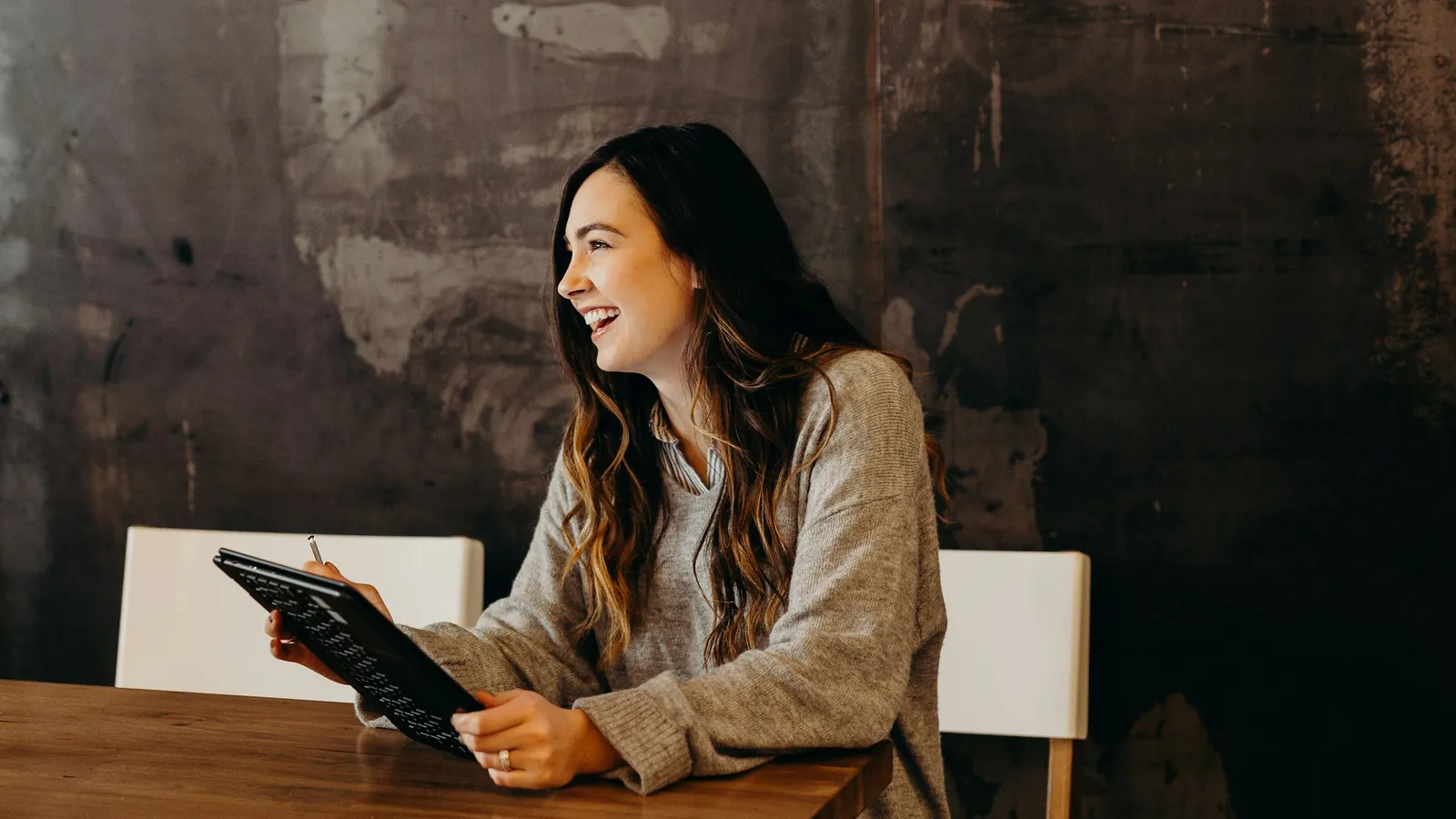 A smiling woman at a café table holding a tablet