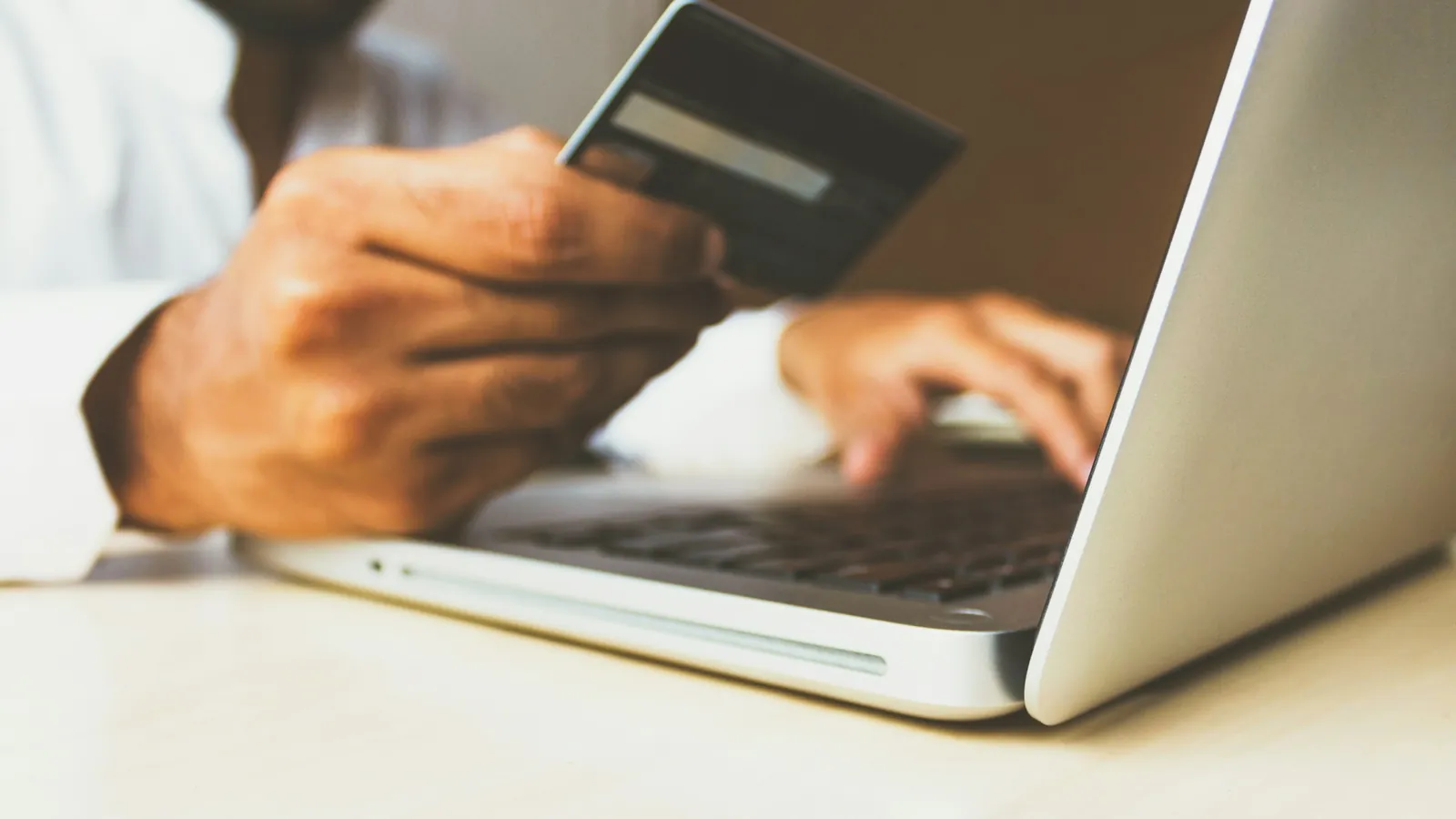 A hand holding a payment card while typing on a laptop