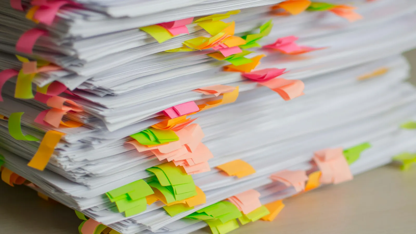 A tall stack of paper documents marked with colorful sticky tabs