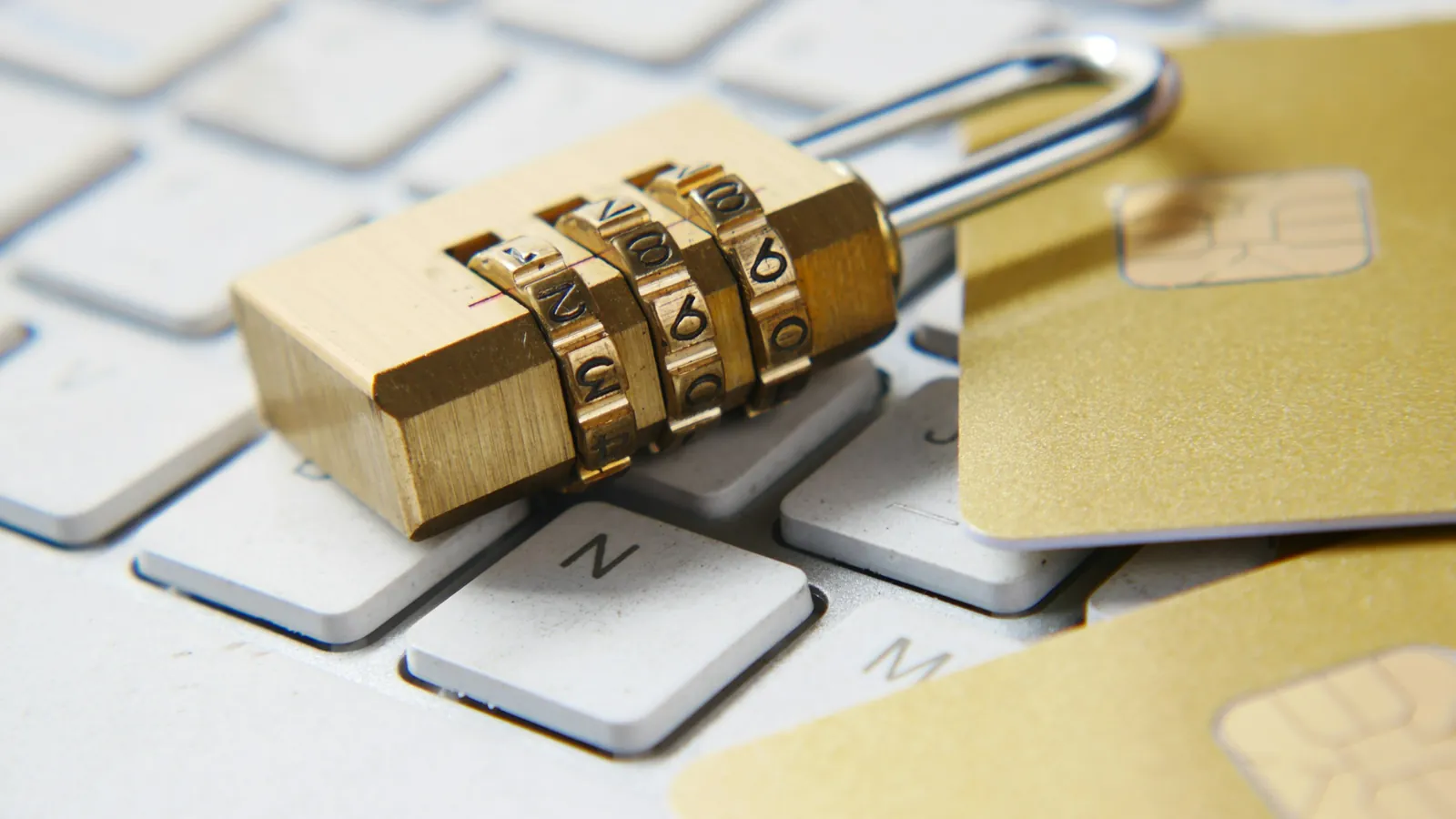 A gold combination padlock resting on a computer keyboard next to a bank card